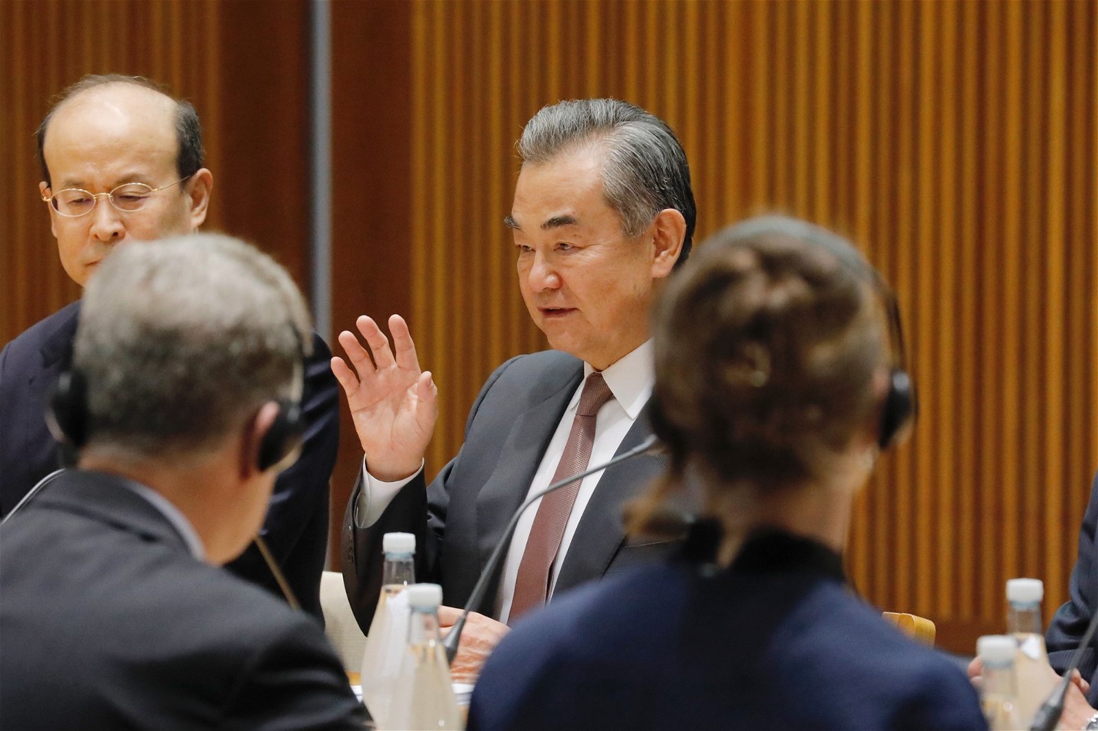 Wang Yi sitting at a table with his hand raised. 