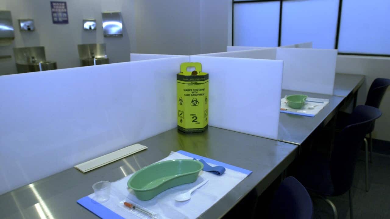 A desk with a low partition.  On the desk is a kidney-shaped green bowl, a syringe in a plastic package and a plastic spoon all resting on a white placemat.