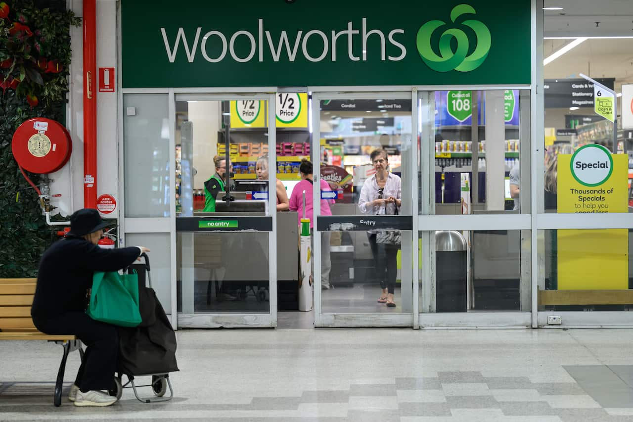 A person sitting on a bench out the front of a Woolworths store.