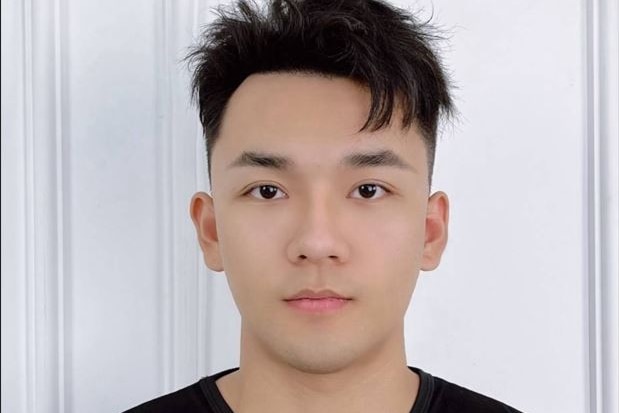 A Chinese man wearing a black muscle tee staring emotionless at the camera on a white door backdrop