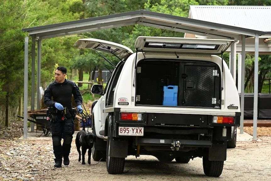 A policeman and police dog next to a police vehicle in a driveway.