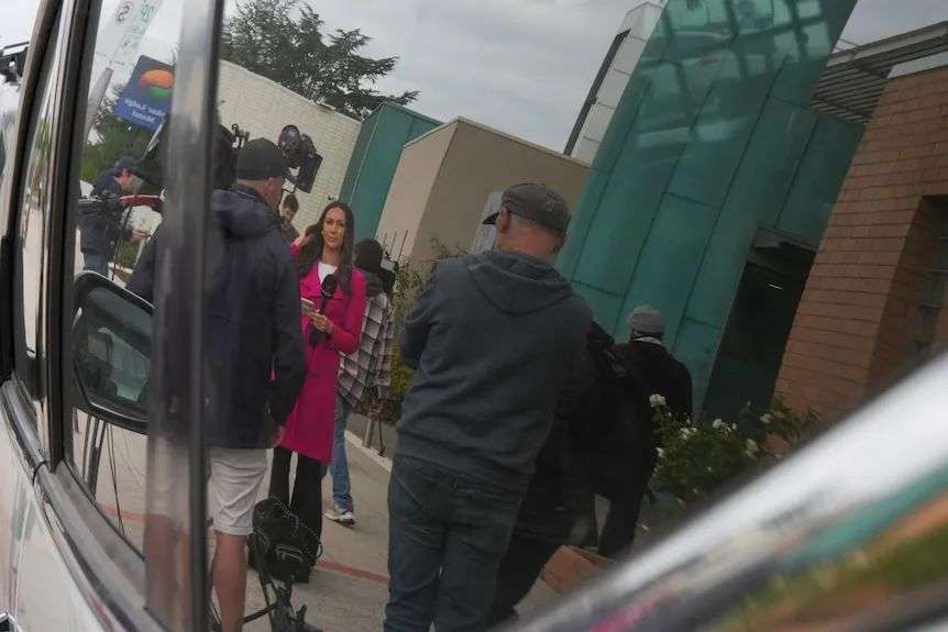 A photo of media crews seen in the reflection of a car window outside a courthouse in Morwell.