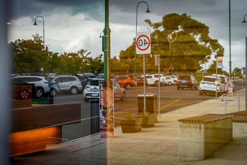 A picture of traffic and parking shown in the reflection of a street window.