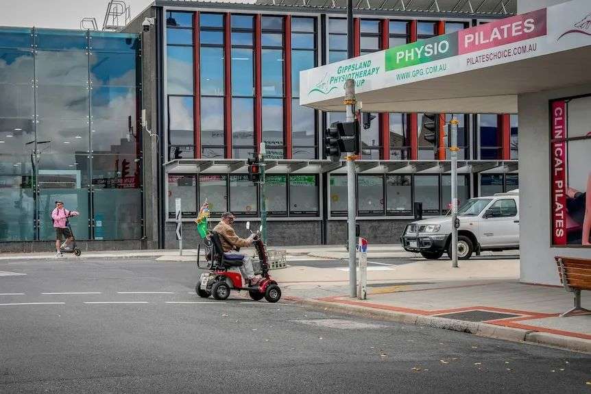 A man on a motorised scooter crosses the street in a regional city centre.