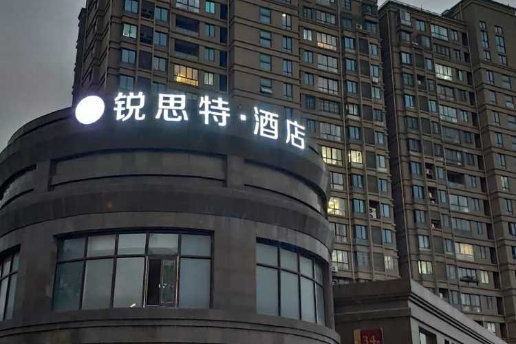 A grey hotel with a white neon sign.