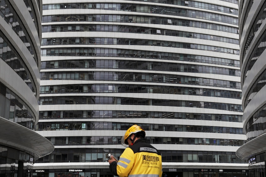 A delivery driver checks their phone in front of large office buildings.