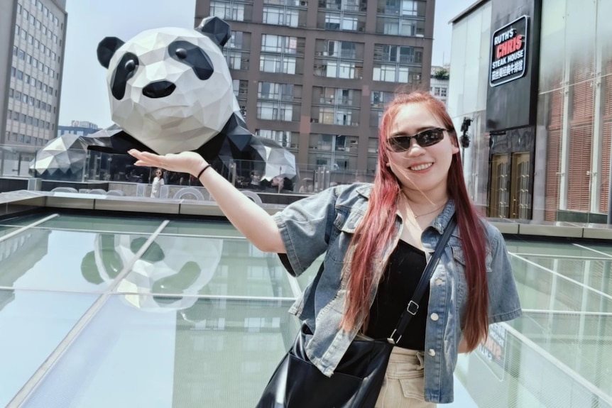 A woman poses on a rooftop with a giant panda sculpture in the background.