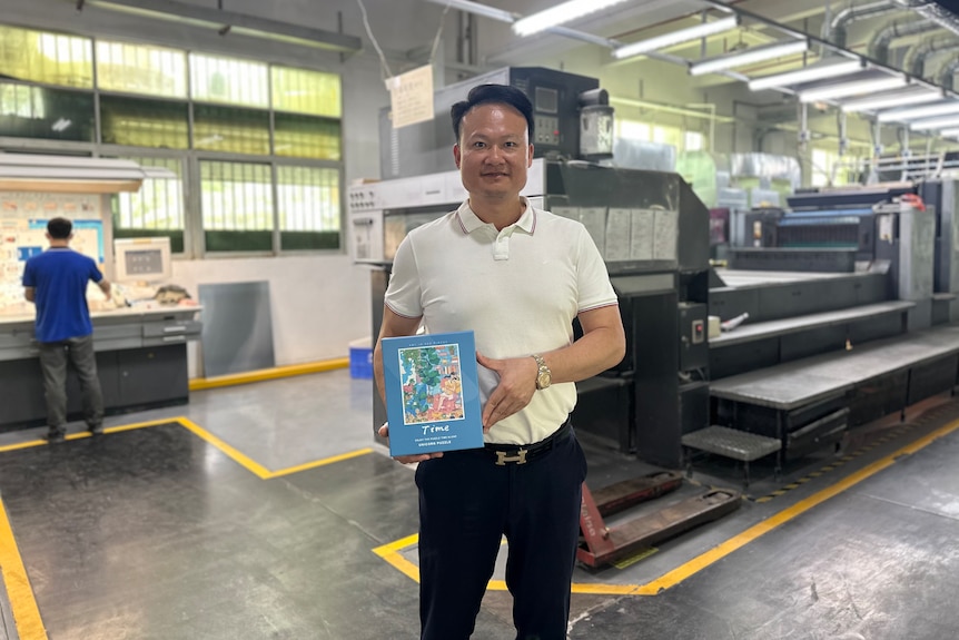 A man in a white T-shirt holding a box of jigsaw puzzles
