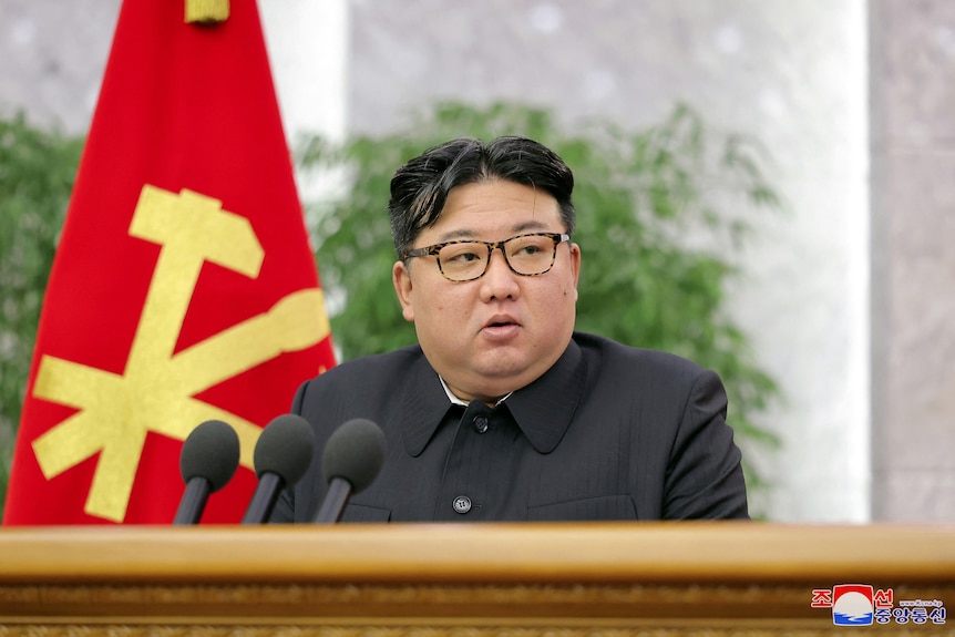 金正恩在麦克风前发表讲话，背景是一面红黄相间的旗帜