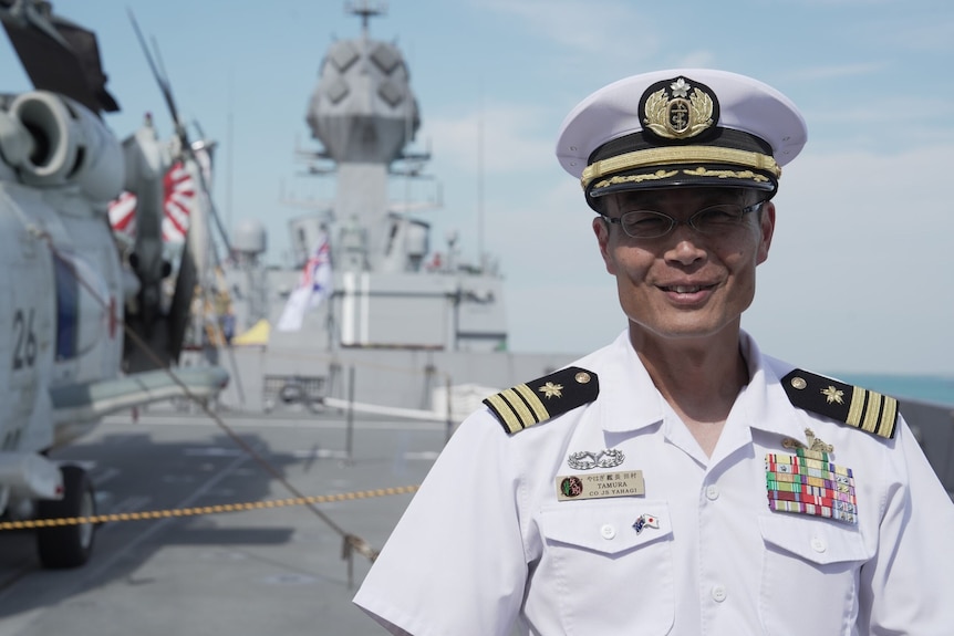 Japanese navy boss stands in front of frigate and smiles 