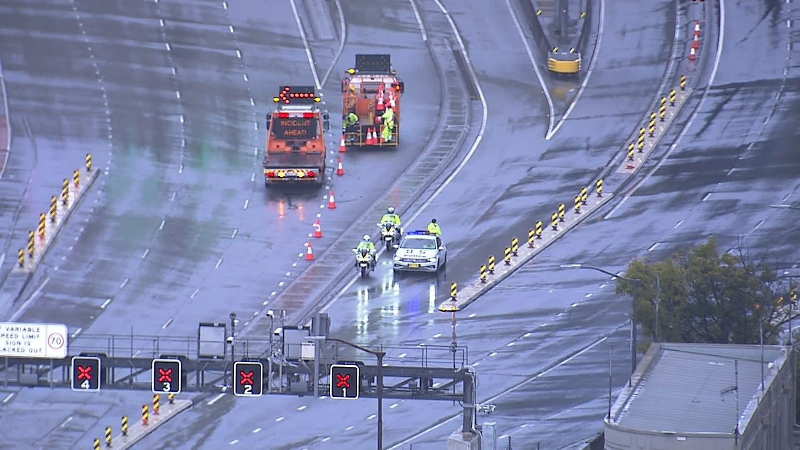 Police vehicles parked on wet approach to bridge.