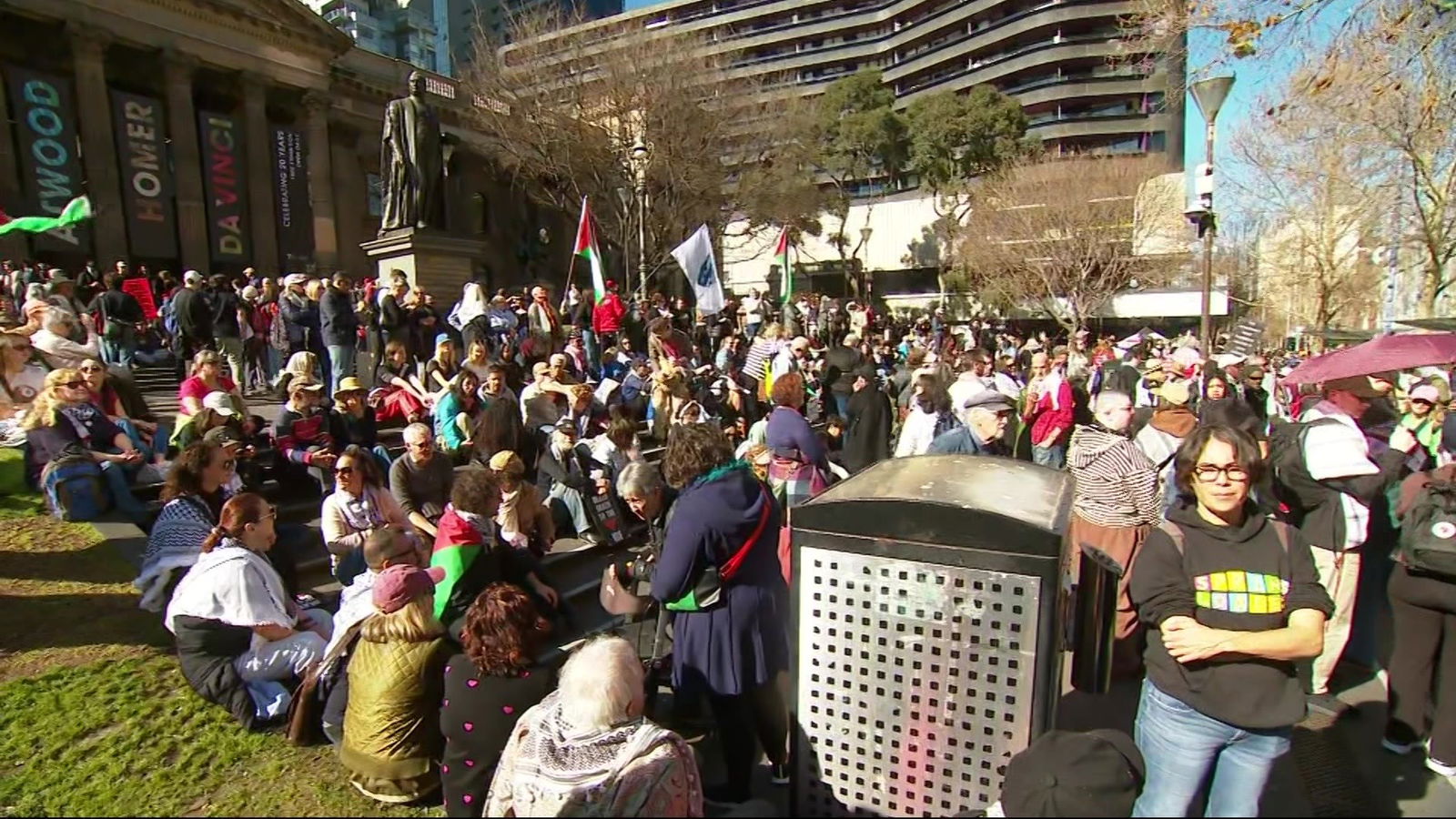 一大群人坐在图书馆的草坪上,手里举着旗帜和标语。