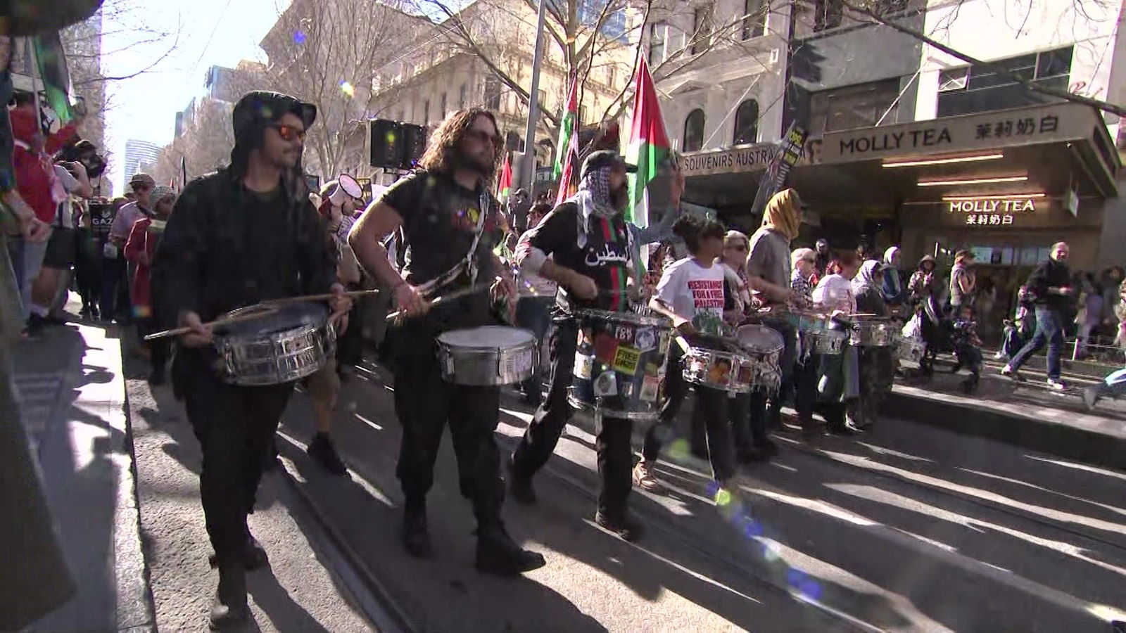 人们排成一排,敲着鼓,后面跟着一大群举着旗帜的人。