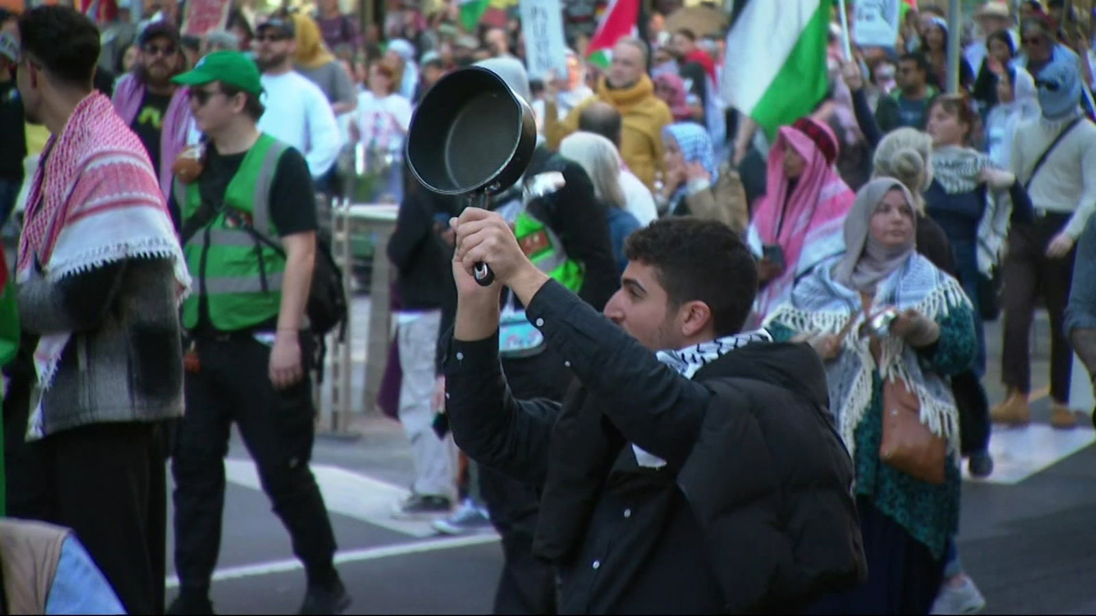 一名男子举着平底锅,与手持巴勒斯坦国旗的人群一起行走。