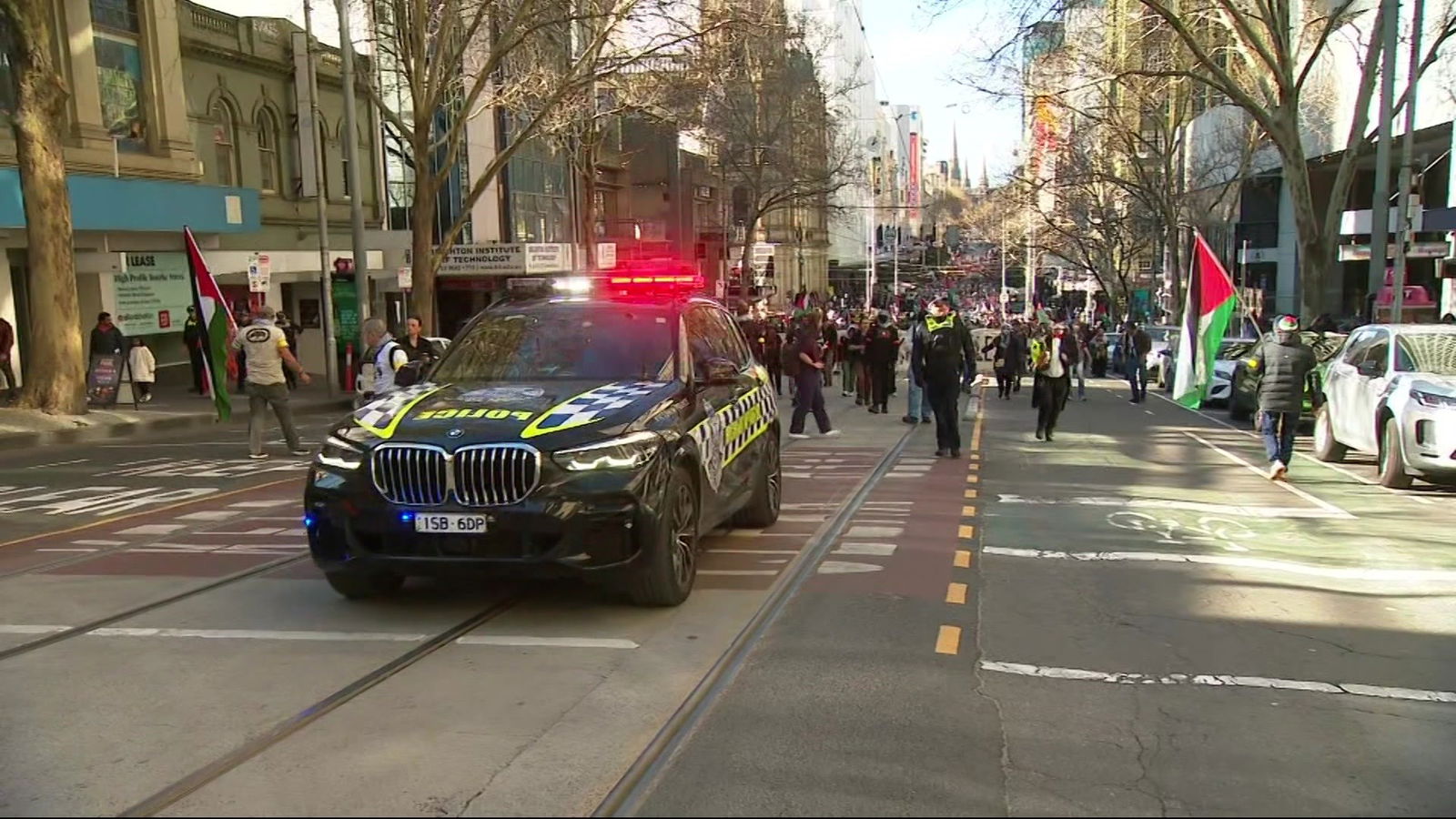 一辆警灯亮着的警车在城市街道上行走的一大群人前面行驶。