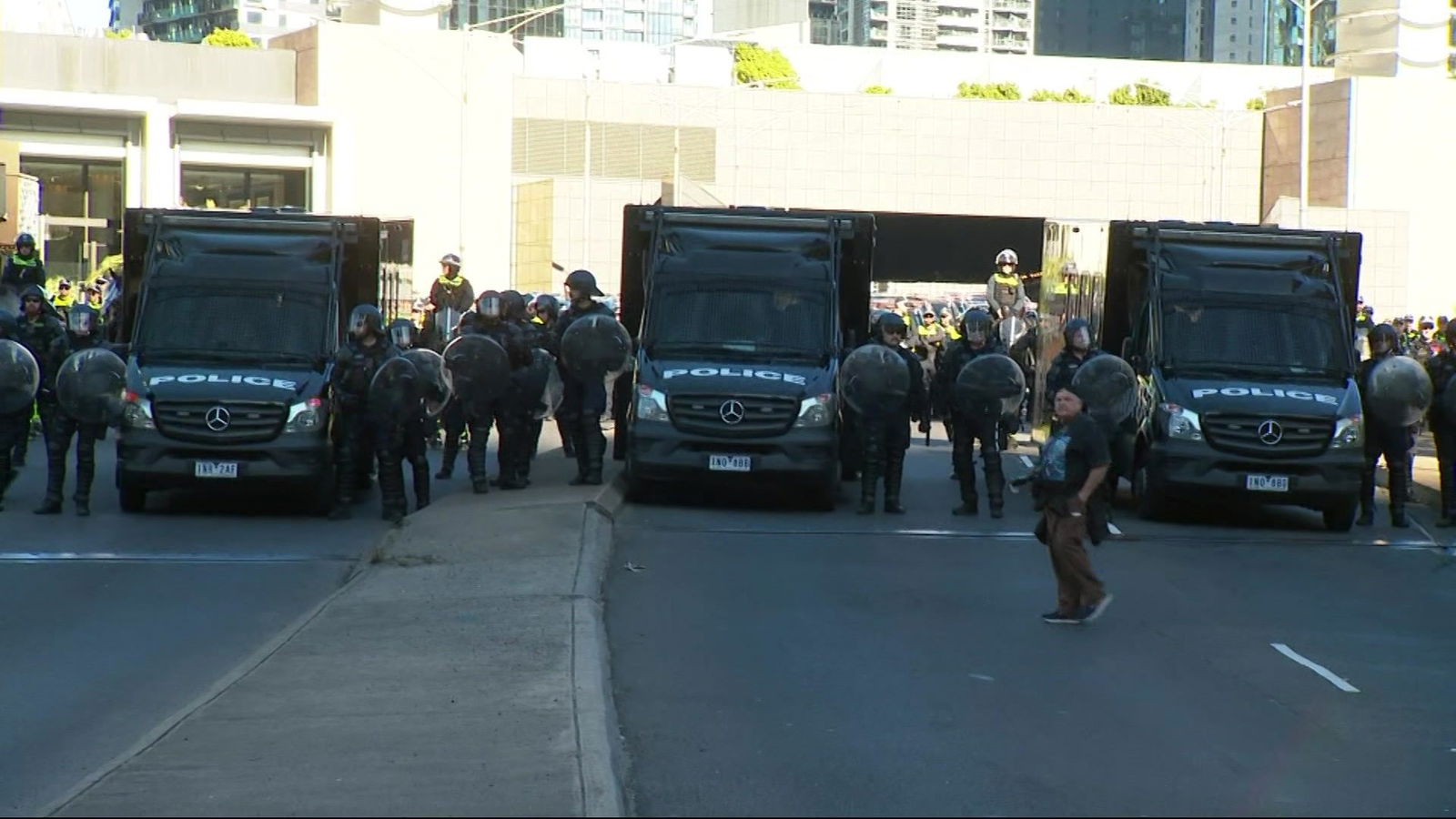 戴着头盔、手持盾牌的警察站在街道上的三辆黑色货车之间。