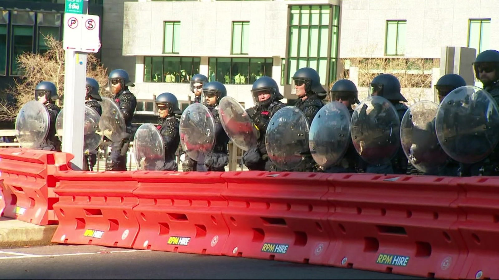 头戴头盔、手持盾牌的警察站在橙色路障后面。