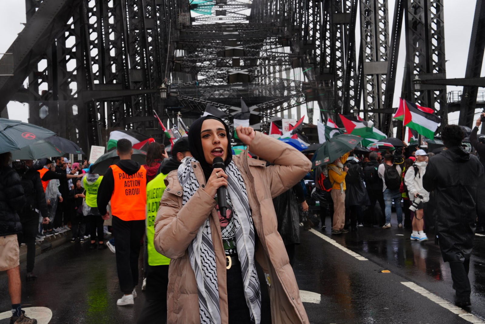 一位身穿米色羽绒服和头巾的女士举起拳头对着麦克风讲话