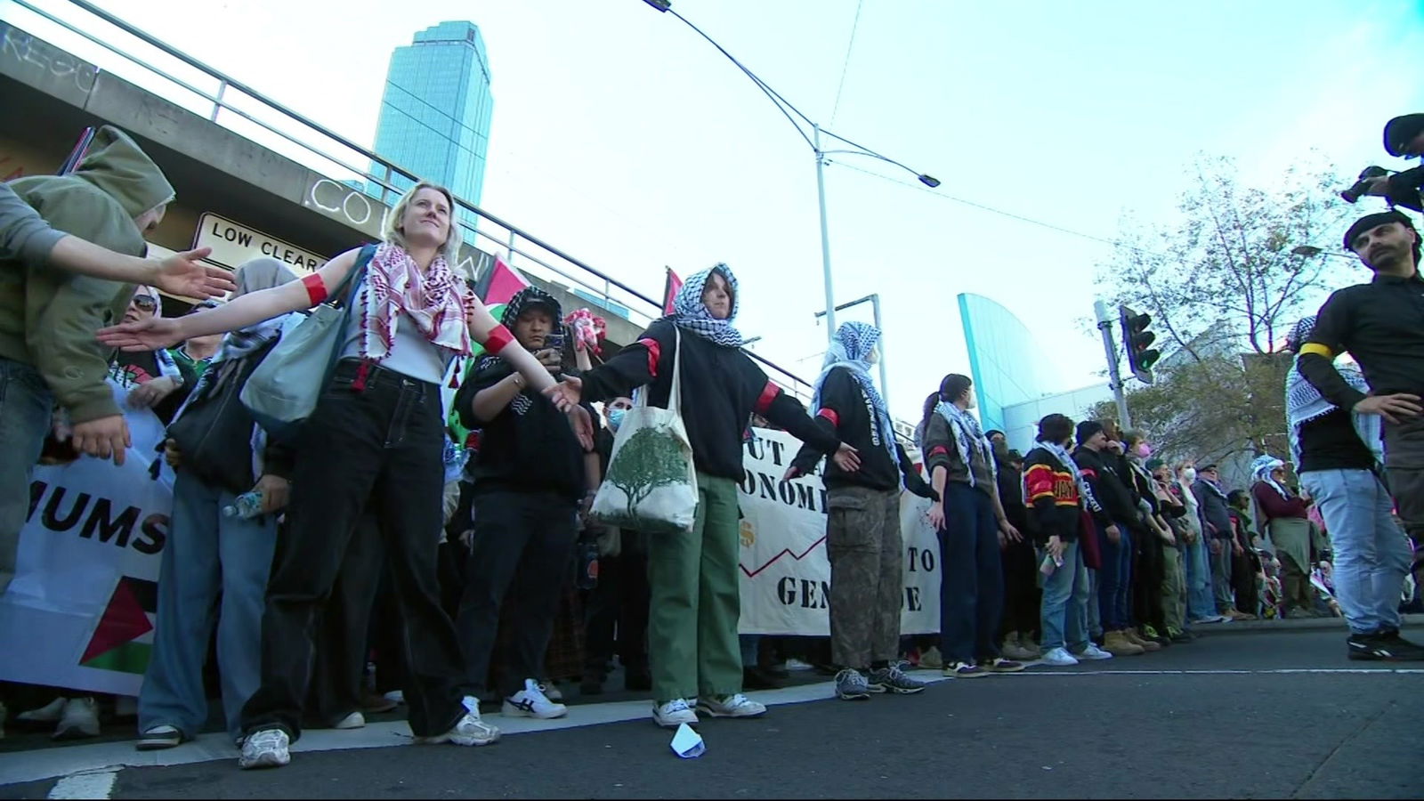 People wearing black and white and red and white scarves spread out their arms, holding hands across a roadway.