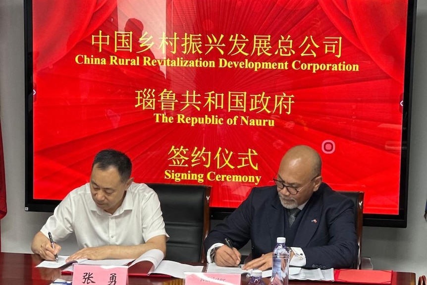 Two men sign a document at a table.