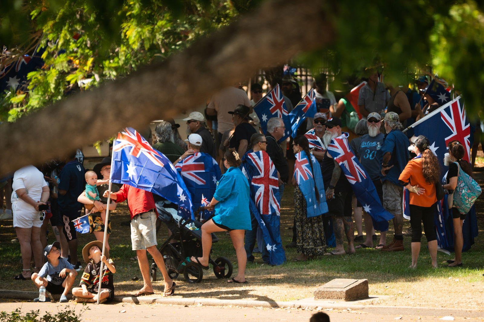 一群人每人手里拿着一面澳大利亚国旗,有些人把国旗像斗篷一样披在背上——这是从远处拍摄的照片。