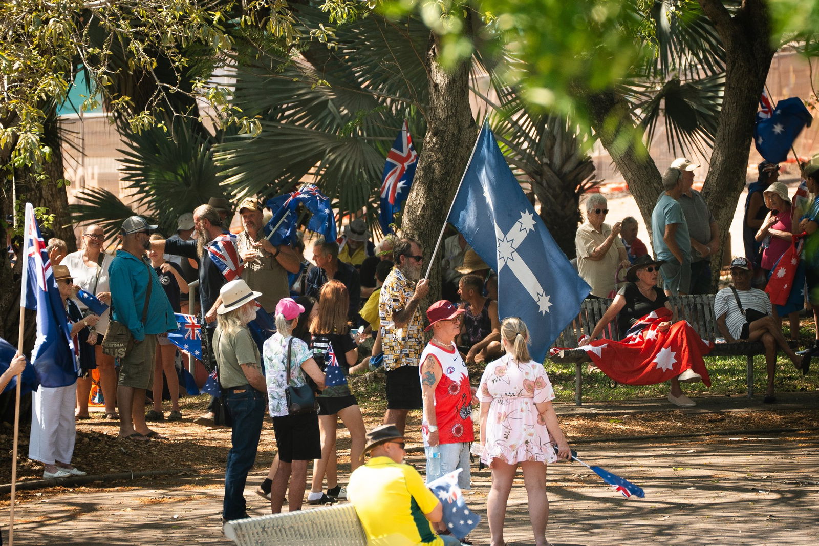 一群人站在公园里,其中一些人手里拿着澳大利亚国旗。一个人拿着一面尤里卡旗,另一个人则把一面红旗搭在腿上。