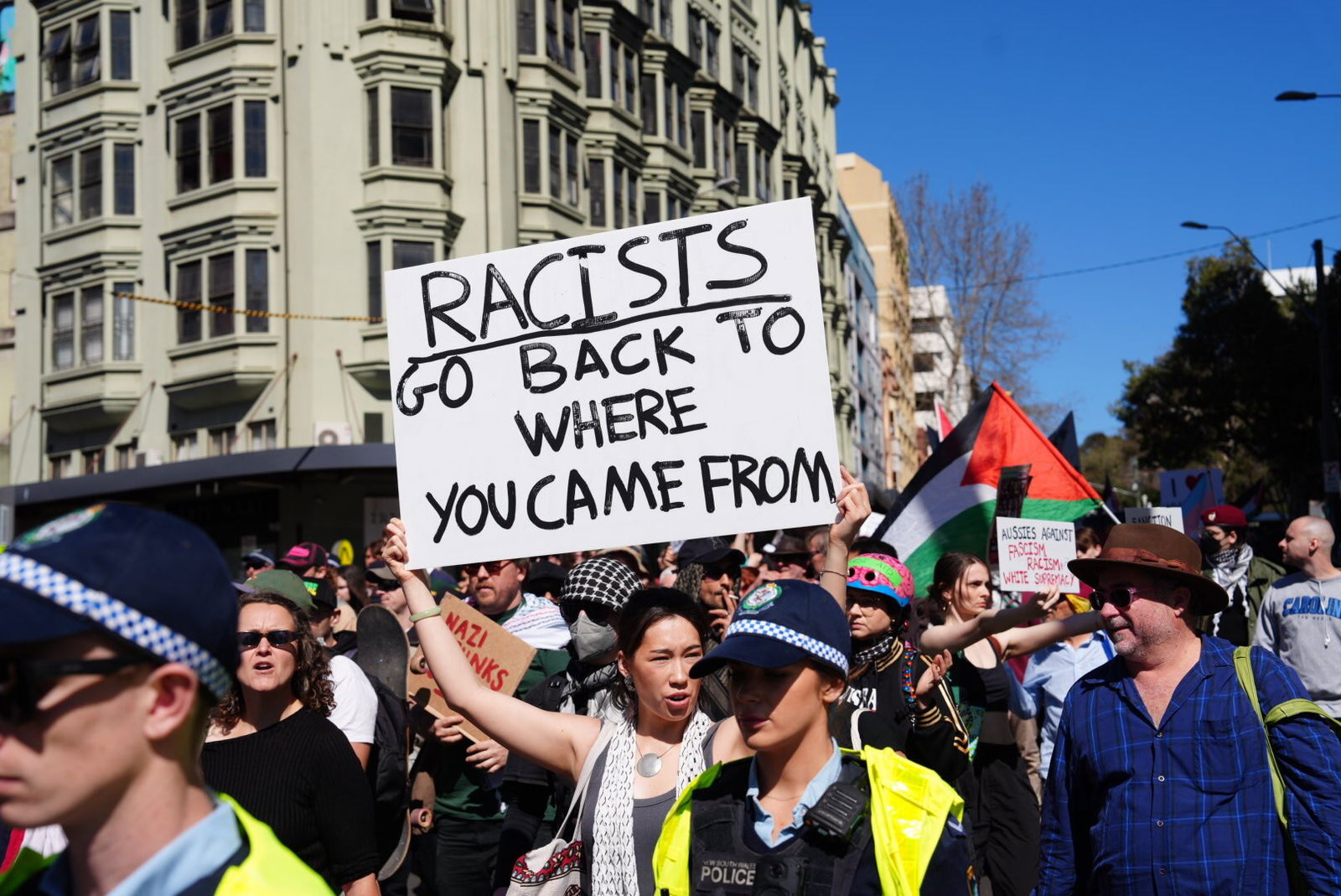 一名年轻女子举着一块牌子,上面写着“种族主义者:滚回你们来的地方去”。
