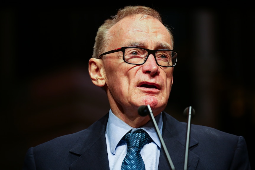 A man wearing a suit and tie talks into a microphone