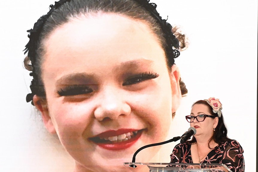 Emma Mason speaks in front of a large screen showing an image of her daughter, Tilly.