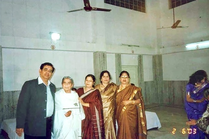An elderly woman standing with four middle aged women and man.