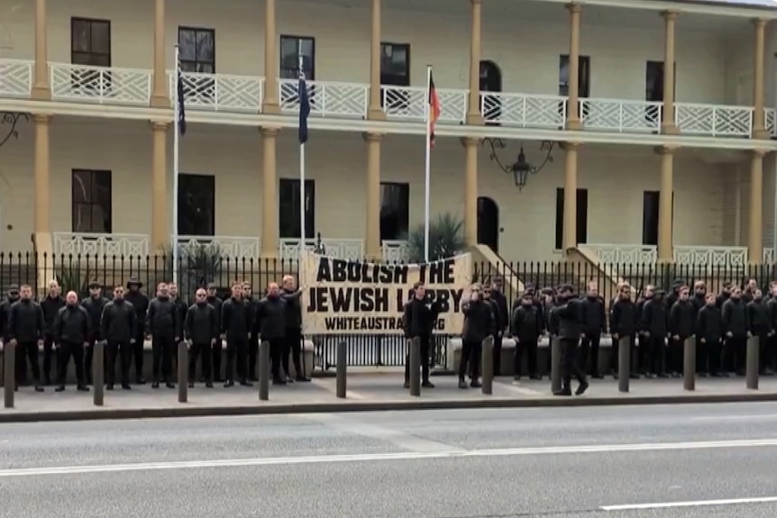 a groupd of about sixty people from the National Socialist Network dressed in black at a rally outside parliament house sydney