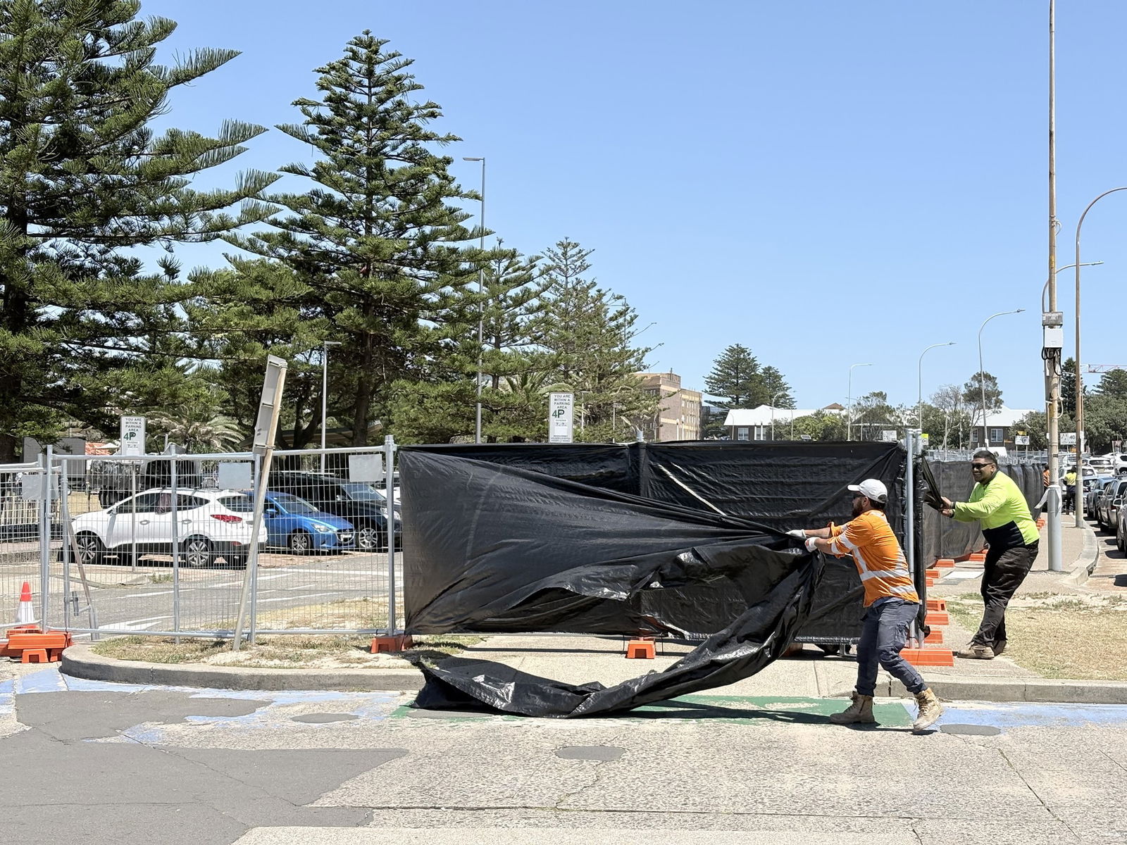 两名身穿高能见度背心的工人从犯罪现场移除钢制围栏和黑色防水布。