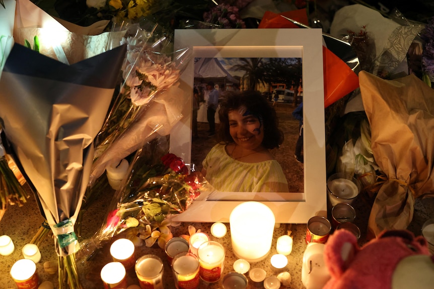 A framed photo of a young girl sits among flowers and battery-lit candles at a makeshift memorial