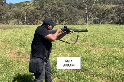 Man holds a rifle in a green field. White text box says Sajid Akram.