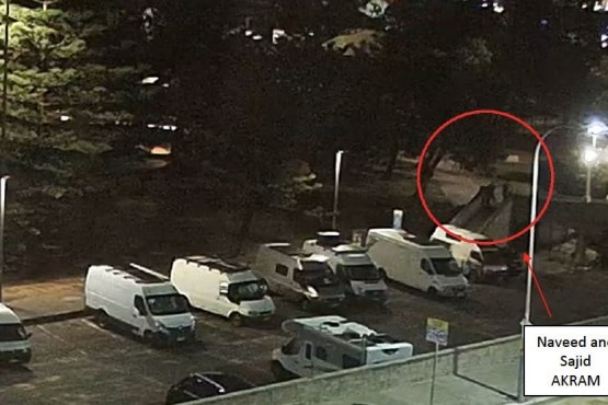 Image of darkened car park. Small silhouettes of figures on bridge.