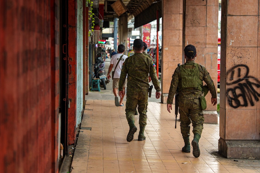 Two military personnel walking down a corridor where some wall pillars have graffiti