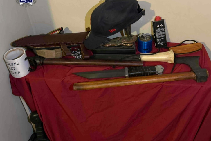 A variety of weapons sittin on a table and on a red piece of material.