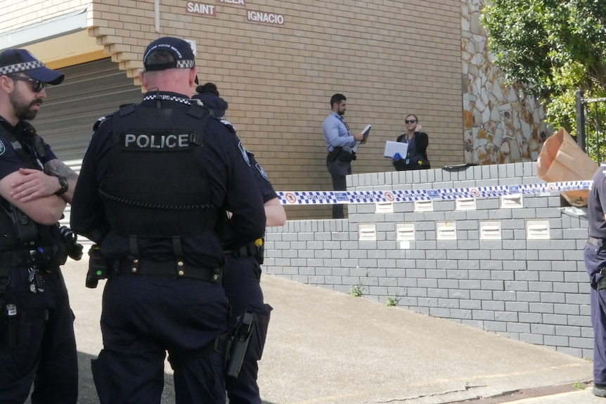 Police officers gather in front of a unit complex, with police tape across a crime scene.