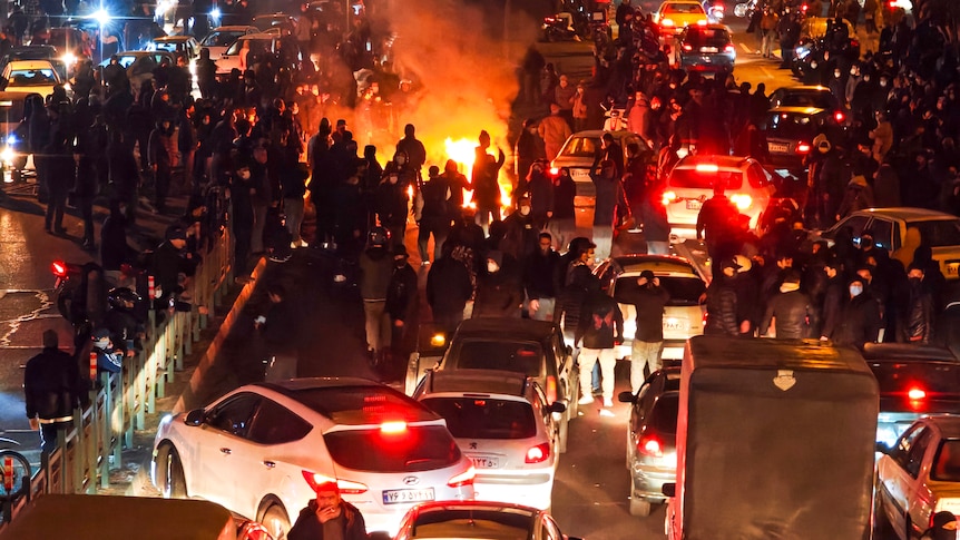 Crowds of people on a road around a fire with cars surrounding them