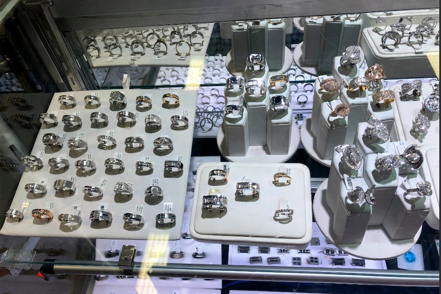 A display cabinet showing dozens of jewel-encrusted rings placed in lines on white pads and stands