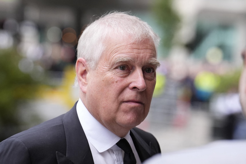 A close up of Andrew Mountbatten Windsor with a neutral expression as he listens to someone speak