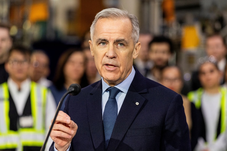 Mark Carney speaks in front of a group of workers in hi-vis vests.