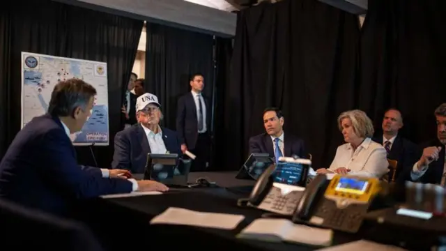 美国总统特朗普戴着一顶白色写上“USA”的帽,坐着聆听中央情报局局长约翰·拉特克利夫(John Ratcliffe)的讲话,同桌者包括美国国务卿马可·卢比奥(Marco Rubio)和白宫幕僚长苏西·威尔斯(Susie Wiles)。