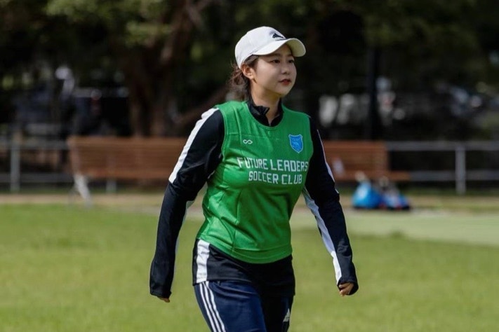 A woman in her 30s in sports uniform walking in a football field