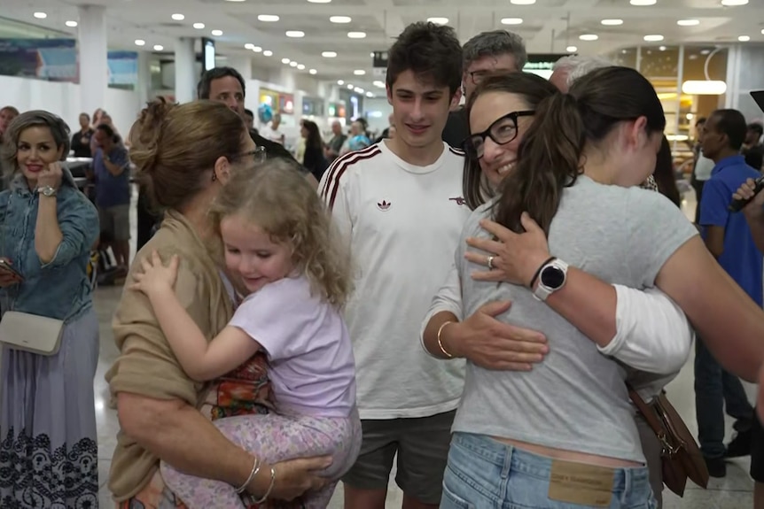 Family members hug in a crowded airport lounge.