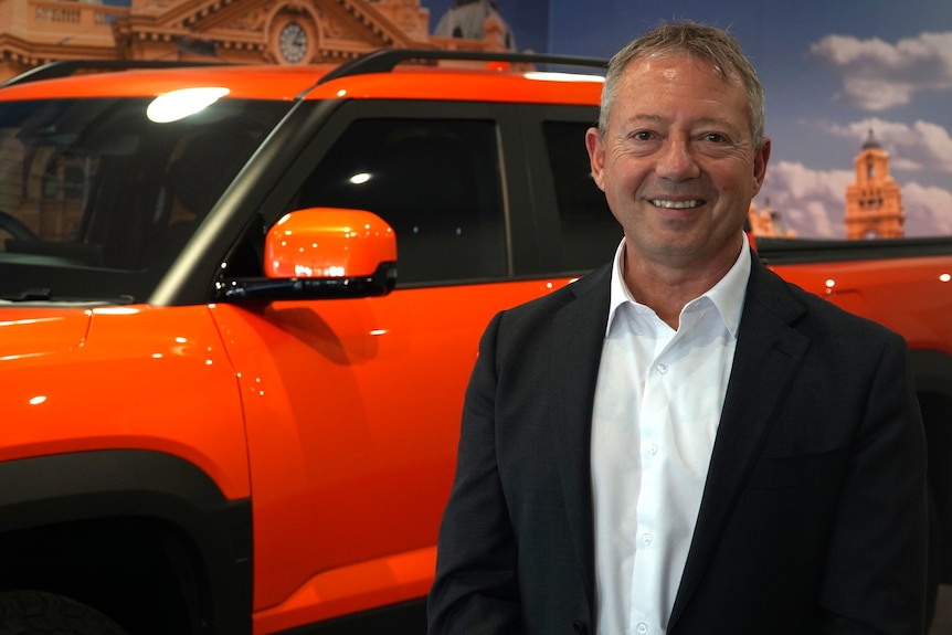 a man in suit standing beside a car in a dealership showroom