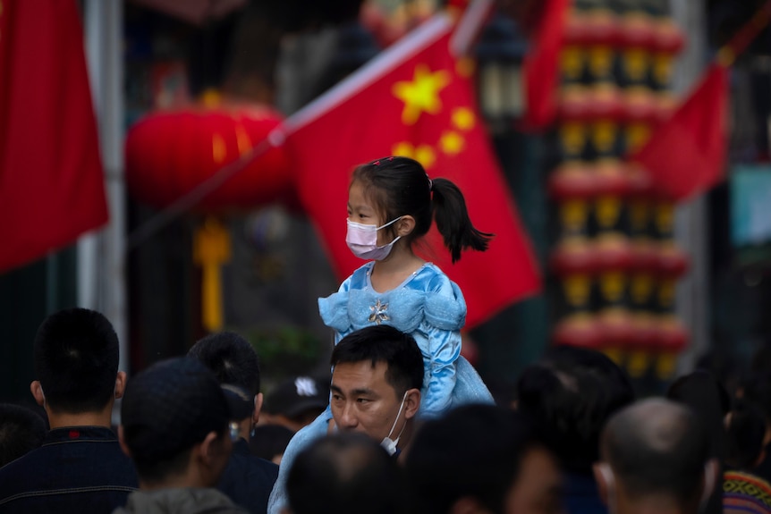 A girl wearing a face mask rides on a man's shoulders as they walk along a tourist shopping street in Beijing.