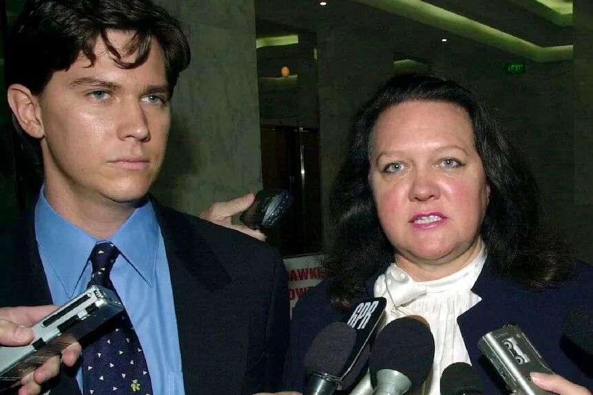 A young man stands with an older woman in front of microphones.