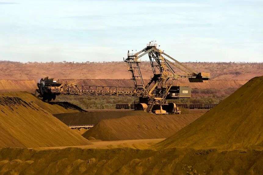A very large mining machine works in an area of red dirt.