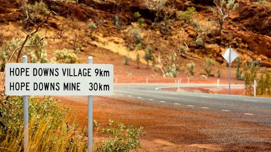 Red dirt at the side of the road with a sign that says 'Hope Downs mine 30km'